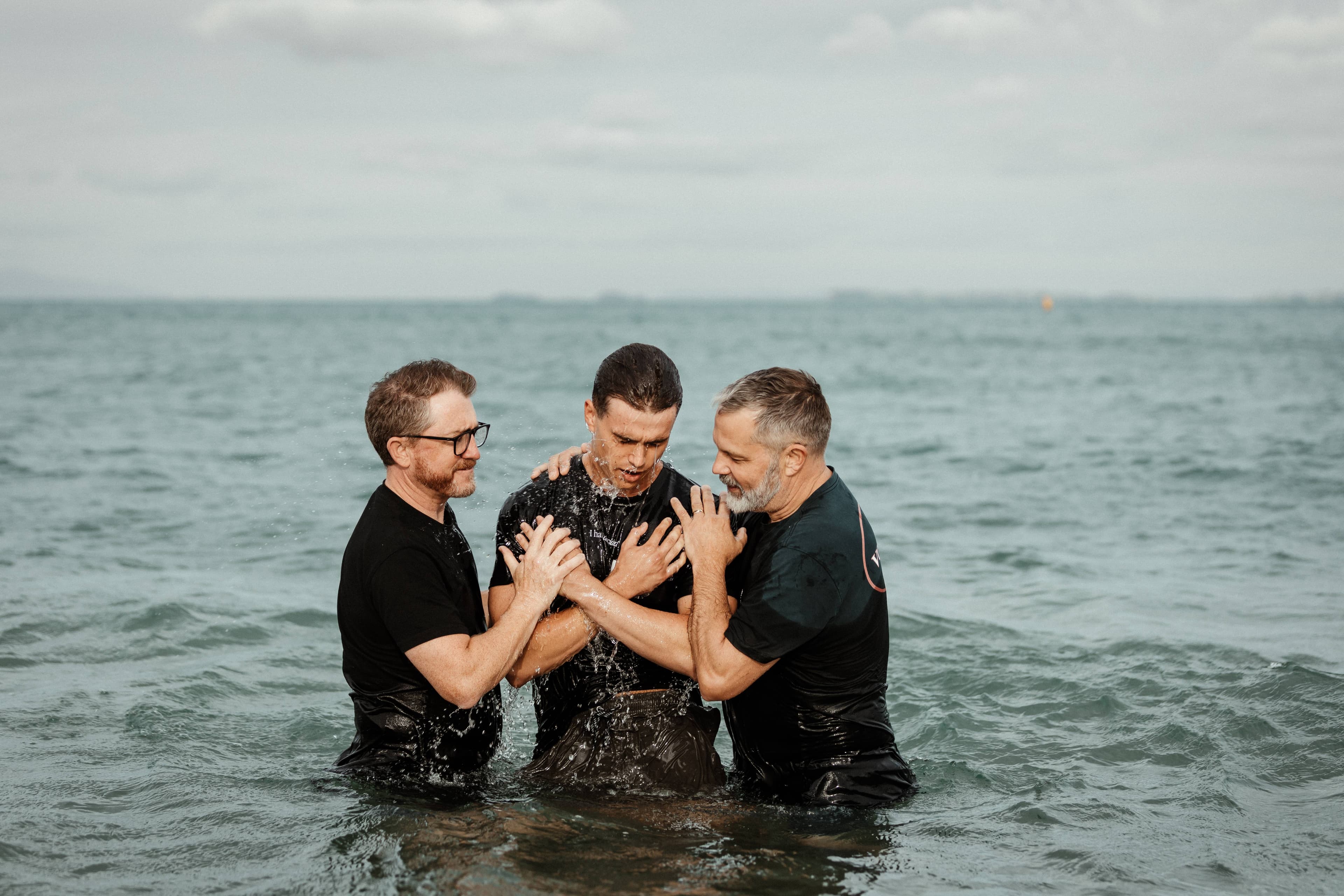 A man who has just been baptised by two men in the ocean