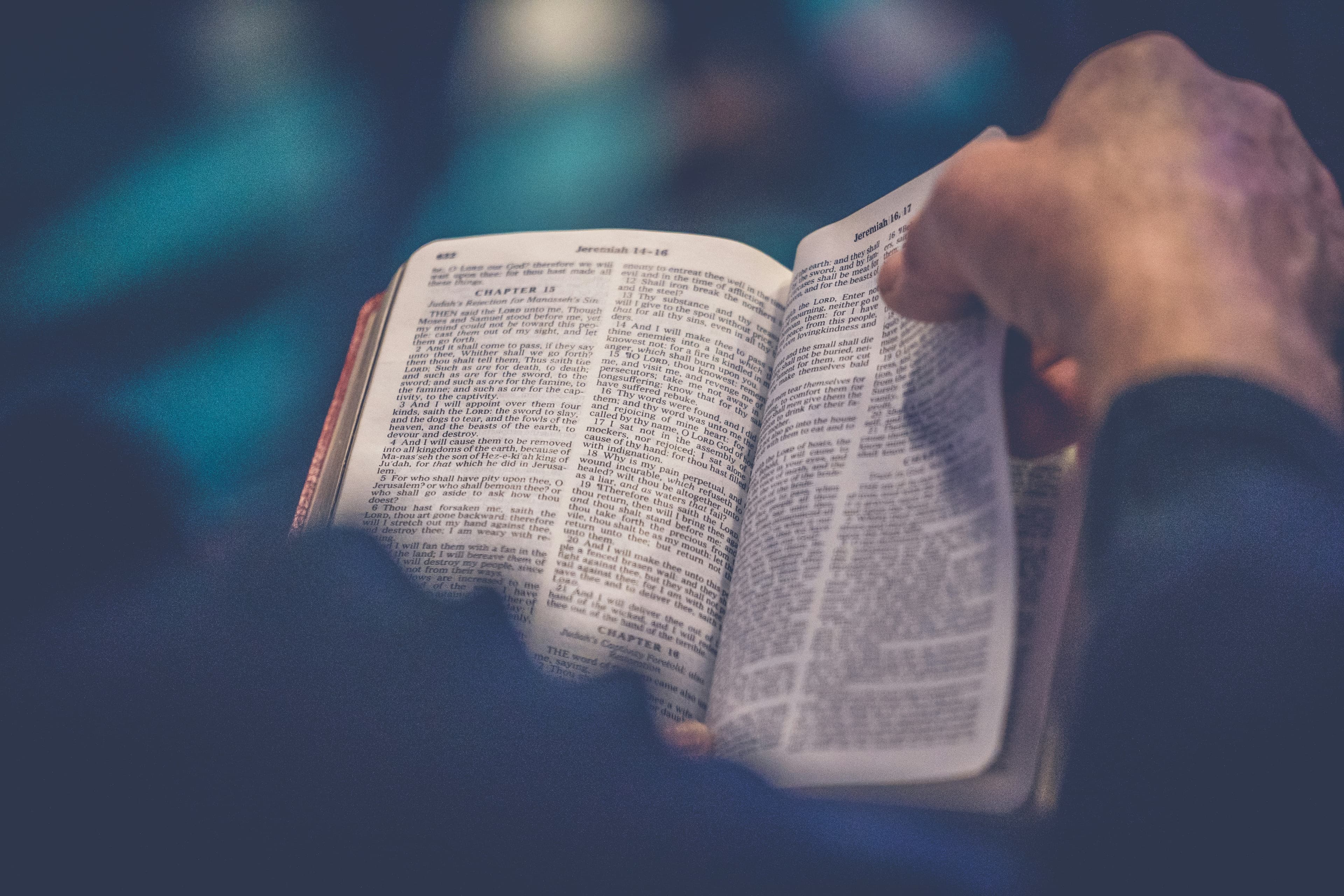 Close up of the bible with a hand holding the page corner in the top right-hand corner