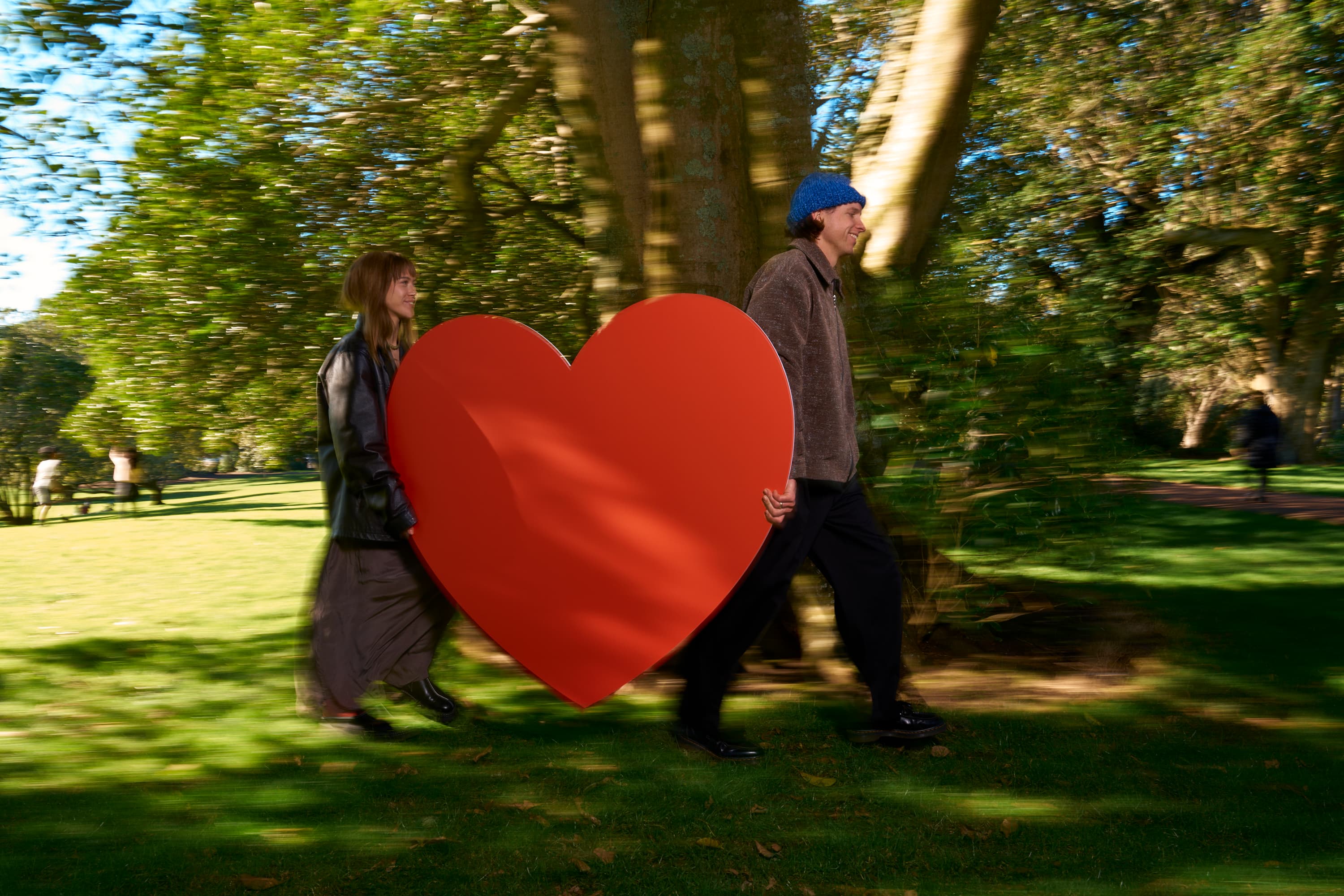 Couple walking from left to right carrying a huge red cardboard heart between them